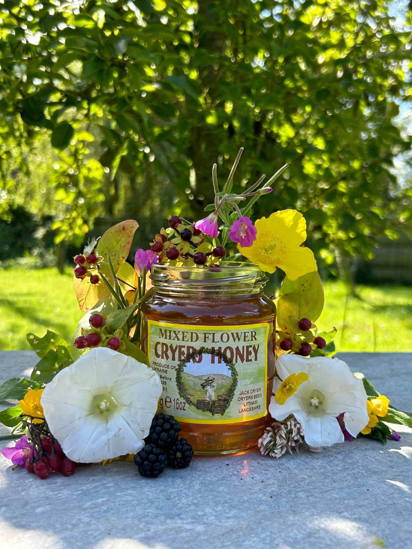 Close-up of a Ukrainian Mixed Flower Honey jar displayed outdoors, with greenery in the background.