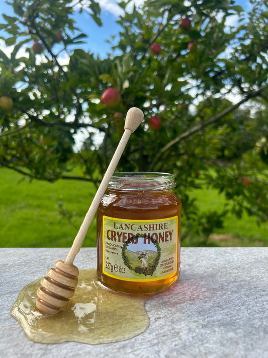 Lancashire Honey jar with honey dipper on a table, showcasing the golden, local honey produced from personal hives.