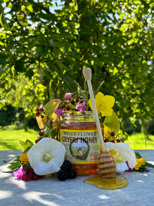 Jar of Ukrainian Mixed Flower Honey surrounded by fresh flowers and fruit in a natural garden setting.